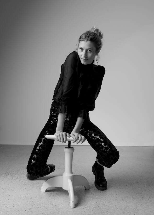 Marta Waydel leaning forward on a stool with an inquisitive expression